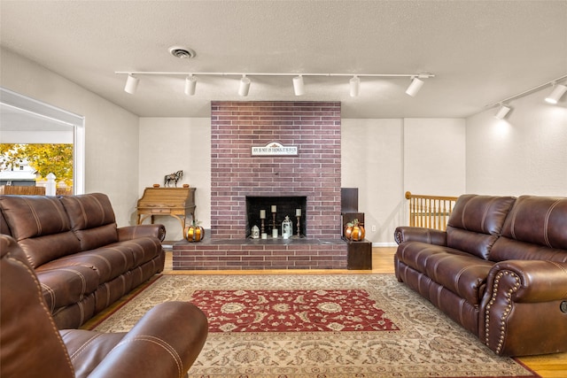 living room with a brick fireplace, light hardwood / wood-style floors, rail lighting, and a textured ceiling