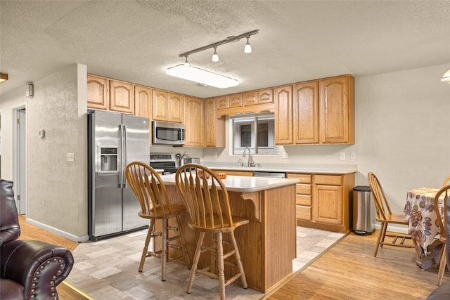 kitchen with stainless steel appliances, a kitchen island, a textured ceiling, a kitchen breakfast bar, and light hardwood / wood-style flooring