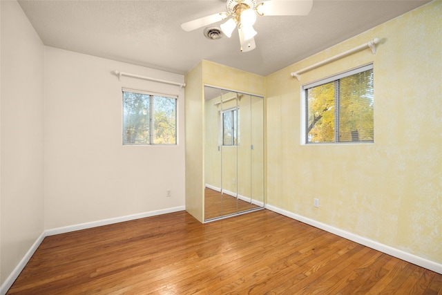 unfurnished bedroom with a textured ceiling, wood-type flooring, ceiling fan, and a closet