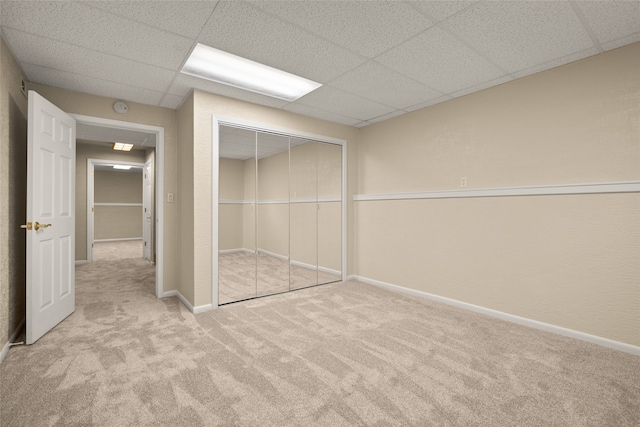 unfurnished bedroom with a drop ceiling, light colored carpet, and a closet