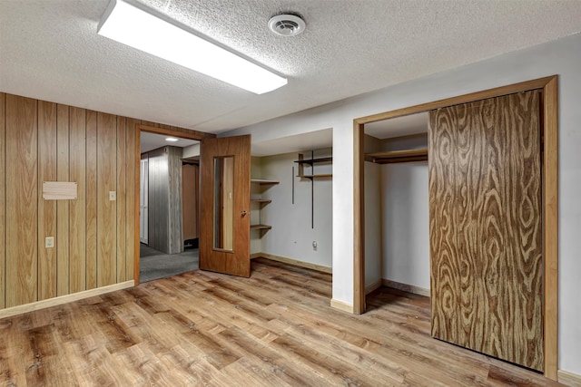 unfurnished bedroom with light hardwood / wood-style floors, a closet, a textured ceiling, and wooden walls