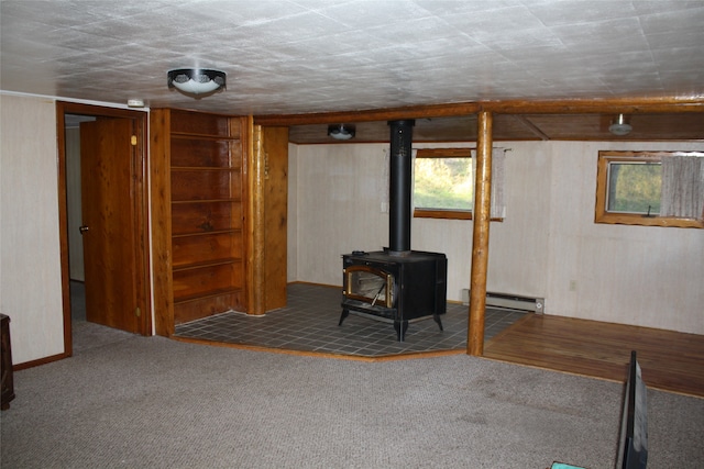 basement featuring a wood stove, baseboard heating, and dark carpet