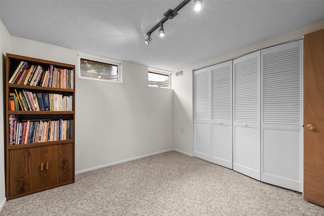 unfurnished bedroom with light carpet, rail lighting, a textured ceiling, and a closet