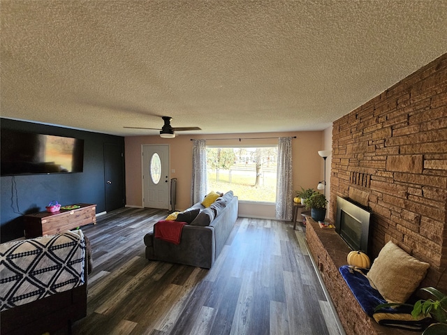 living room featuring dark wood-type flooring, ceiling fan, a textured ceiling, and a fireplace