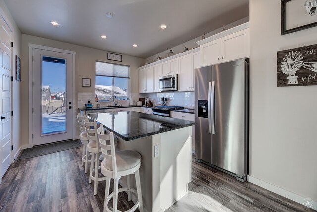 kitchen with stainless steel appliances, white cabinets, hardwood / wood-style flooring, a kitchen island, and backsplash