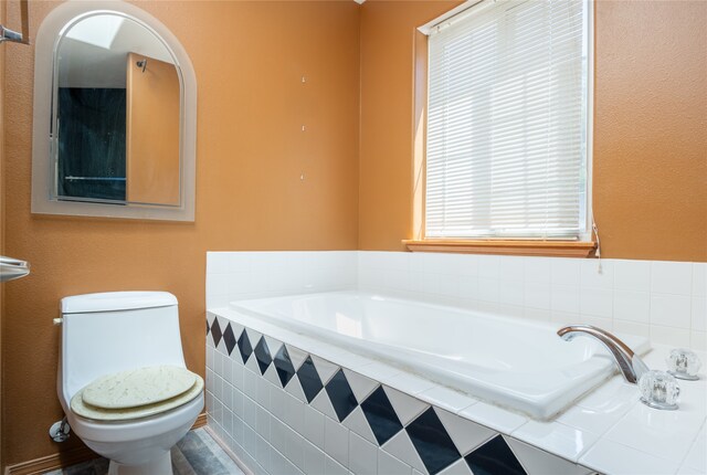 bathroom featuring toilet, plenty of natural light, and tiled tub