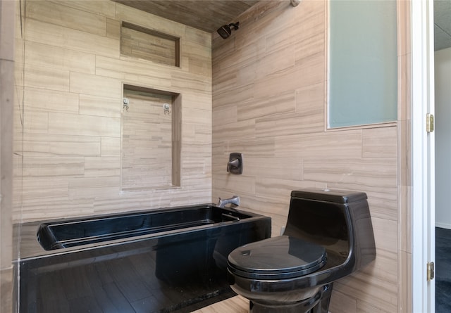 bathroom featuring toilet, a tub, and tile walls