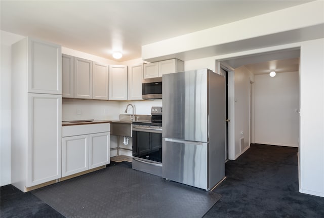 kitchen featuring appliances with stainless steel finishes, white cabinetry, sink, and dark carpet