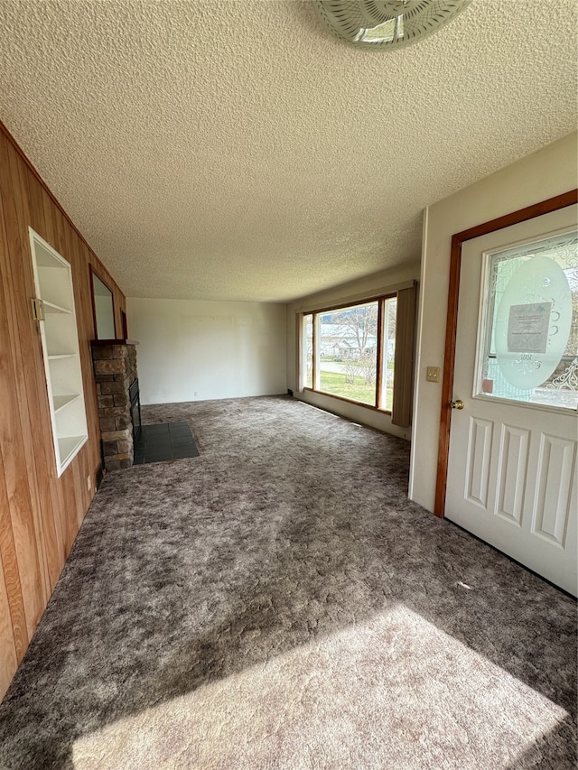 unfurnished living room with dark carpet, a fireplace, a textured ceiling, and wood walls