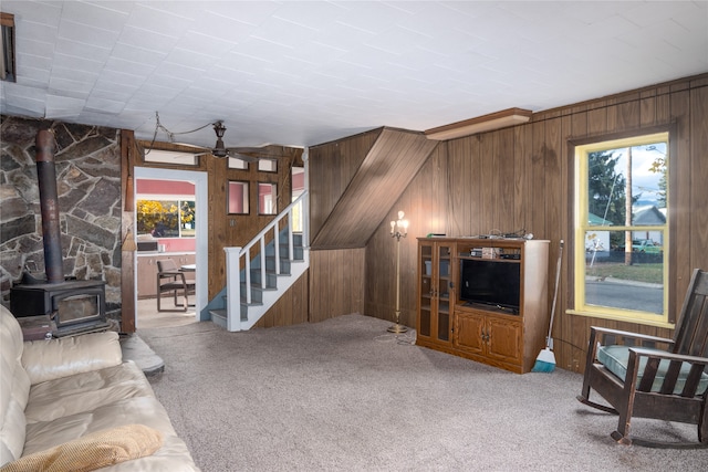 living room with lofted ceiling, wooden walls, a wood stove, carpet, and ceiling fan