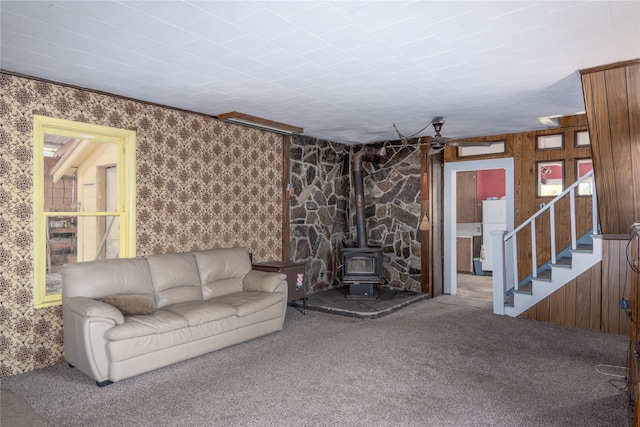 unfurnished living room featuring wooden walls, carpet flooring, and a wood stove