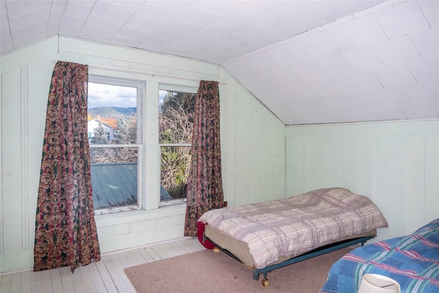 bedroom with light hardwood / wood-style flooring, a mountain view, vaulted ceiling, and wooden walls