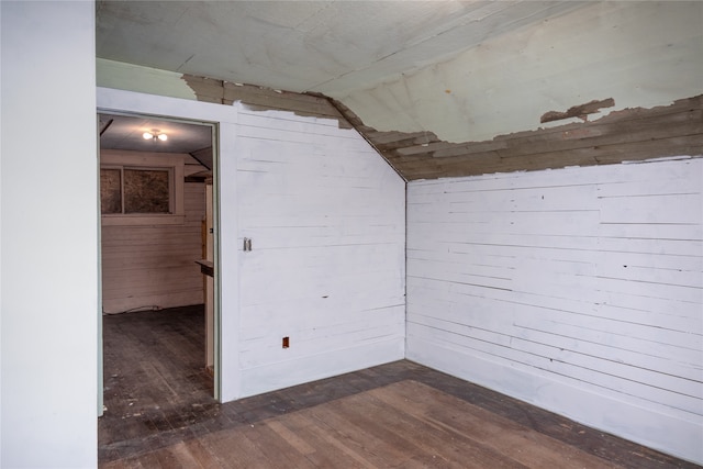 empty room with dark wood-type flooring, vaulted ceiling, and wood walls