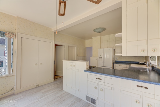 kitchen featuring white fridge with ice dispenser, kitchen peninsula, white cabinets, and sink