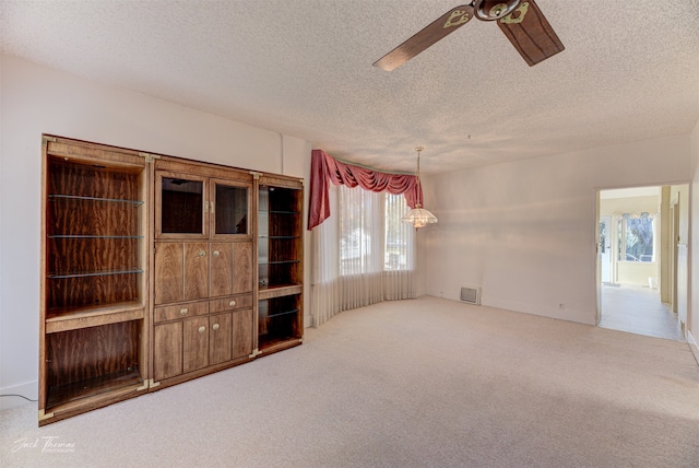 unfurnished living room with a textured ceiling, light colored carpet, plenty of natural light, and ceiling fan