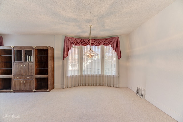 unfurnished dining area with carpet flooring, a textured ceiling, and an inviting chandelier