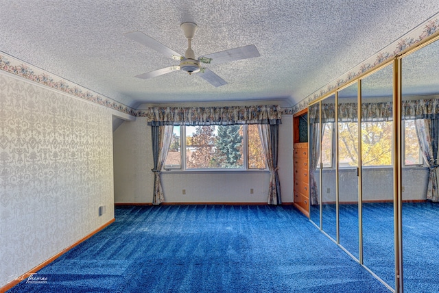 spare room featuring a textured ceiling, dark carpet, and ceiling fan