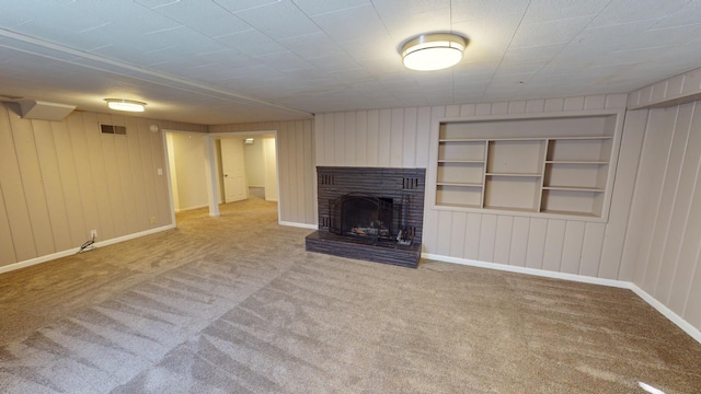 unfurnished living room featuring carpet floors, wooden walls, built in shelves, and a brick fireplace