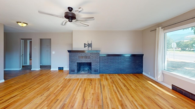 unfurnished living room featuring light hardwood / wood-style floors, a healthy amount of sunlight, a brick fireplace, and ceiling fan