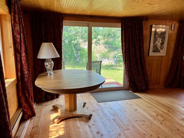 dining area featuring light hardwood / wood-style floors, wood walls, wooden ceiling, and a baseboard radiator