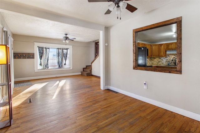 empty room with sink, ceiling fan, a textured ceiling, and light wood-type flooring