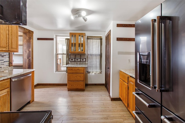 kitchen with appliances with stainless steel finishes, light stone counters, backsplash, and light hardwood / wood-style floors