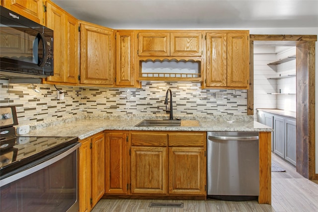 kitchen with appliances with stainless steel finishes, tasteful backsplash, sink, light stone countertops, and light wood-type flooring