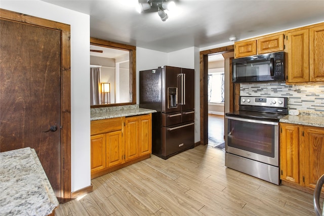 kitchen featuring light stone countertops, backsplash, light wood-type flooring, and black appliances