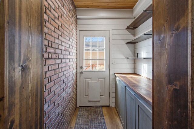 doorway with dark wood-type flooring, wooden ceiling, and brick wall