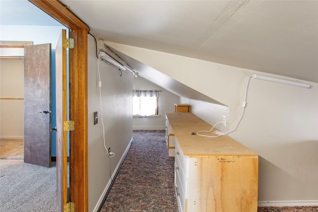 hall with vaulted ceiling and dark colored carpet