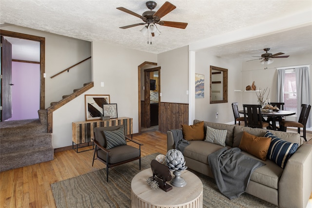 living room with ceiling fan, a textured ceiling, and light wood-type flooring