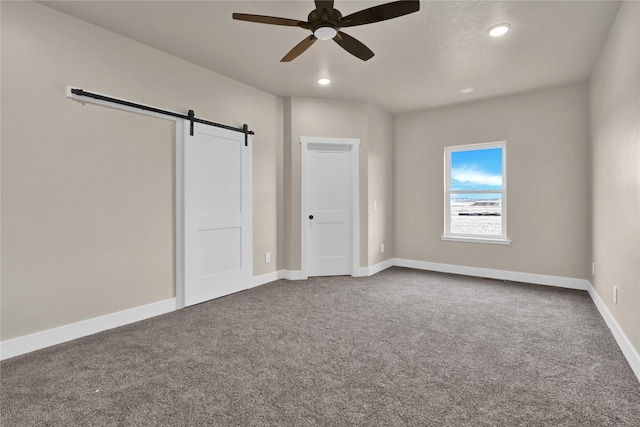 unfurnished bedroom with a barn door, ceiling fan, and carpet