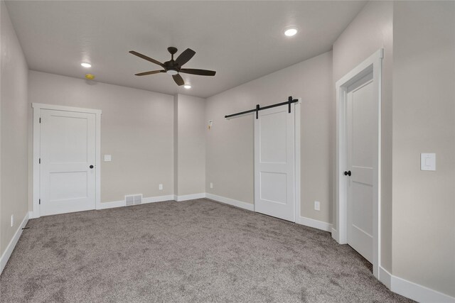 carpeted empty room with ceiling fan and a barn door