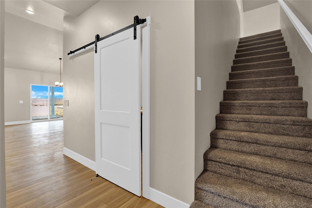 staircase with hardwood / wood-style floors, a barn door, and an inviting chandelier