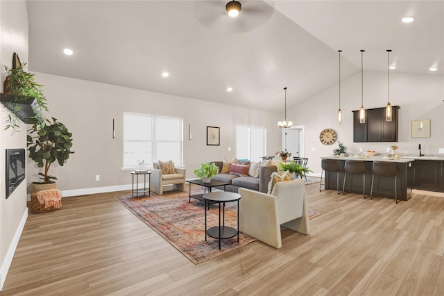 living room with ceiling fan with notable chandelier, light wood-type flooring, and vaulted ceiling