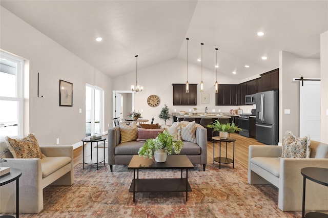 living room featuring a barn door, vaulted ceiling, light hardwood / wood-style flooring, and a notable chandelier