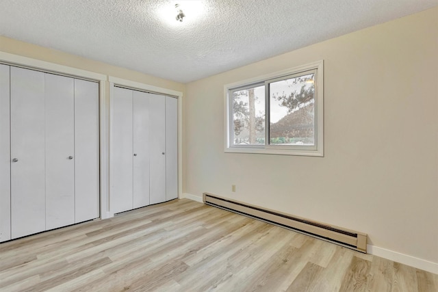 20622 US Highway 10 E, Clinton, MT 59825 - unfurnished bedroom featuring baseboard heating, multiple closets, light wood-style flooring, and a textured ceiling