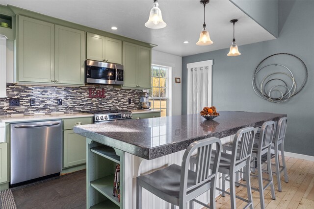 kitchen featuring appliances with stainless steel finishes, a kitchen island, green cabinets, hanging light fixtures, and dark hardwood / wood-style floors