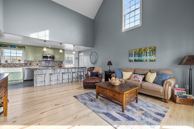 living room with a high ceiling, light wood-type flooring, and plenty of natural light