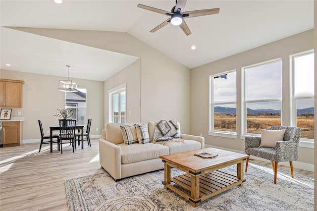 living room featuring a mountain view, vaulted ceiling, light wood-type flooring, and ceiling fan with notable chandelier