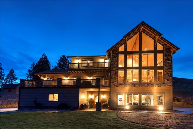 back house at dusk with a patio, a lawn, and a balcony