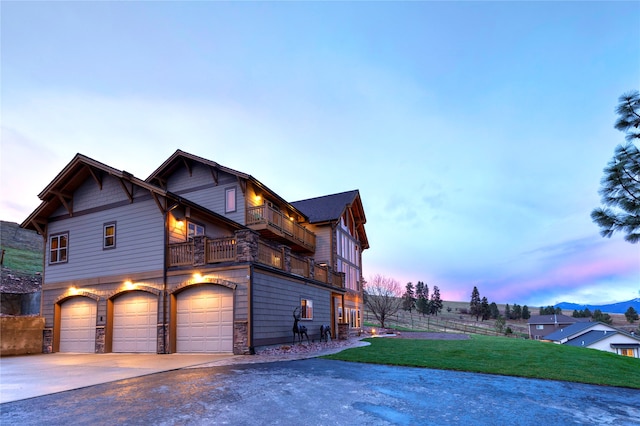 property exterior at dusk featuring a lawn, a balcony, and a garage