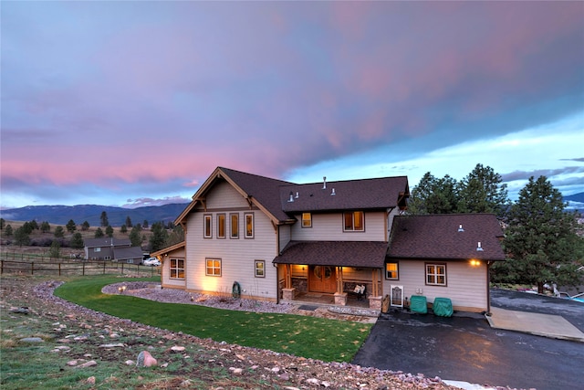 back house at dusk with a mountain view and a lawn