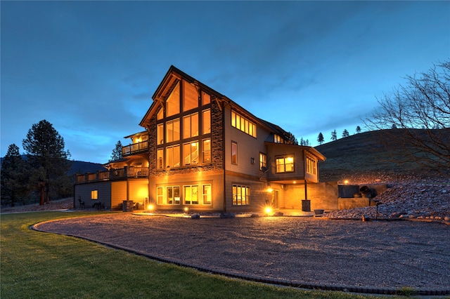 back house at dusk with a balcony and a lawn