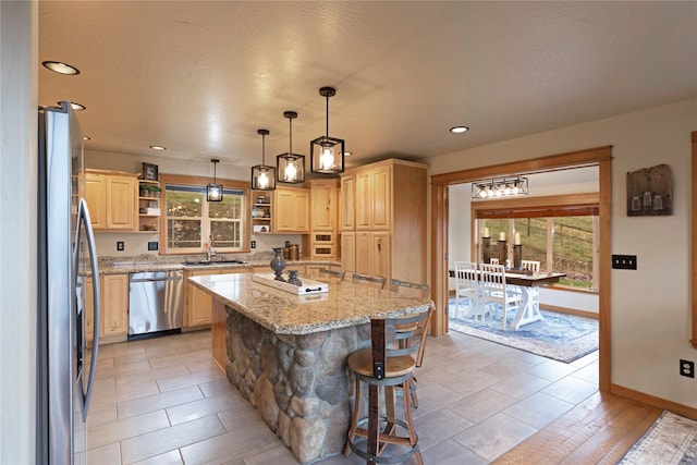 kitchen with a kitchen island, sink, light stone countertops, light brown cabinetry, and appliances with stainless steel finishes