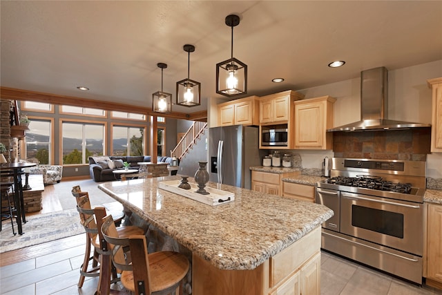 kitchen with a kitchen island, wall chimney range hood, stainless steel appliances, light stone countertops, and pendant lighting