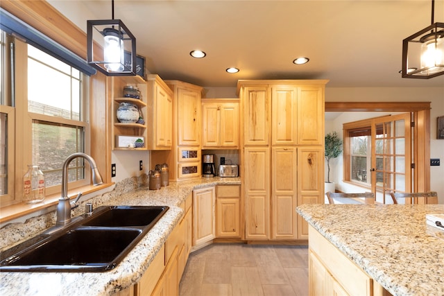 kitchen with light stone counters, sink, light brown cabinets, and hanging light fixtures