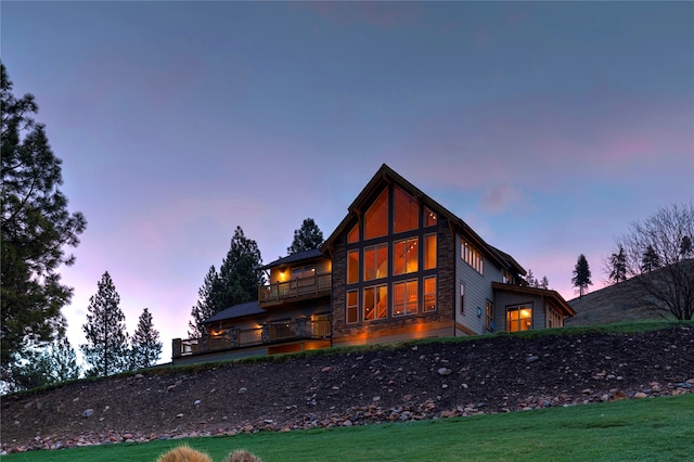 back house at dusk with a balcony and a yard