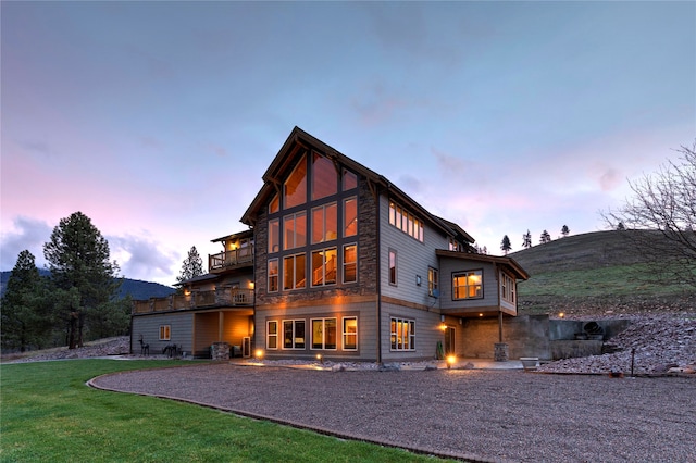 back house at dusk featuring a patio, a yard, and a balcony