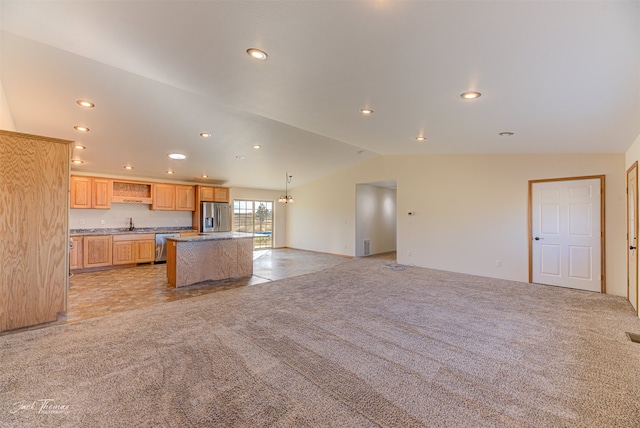 kitchen featuring lofted ceiling, a center island, light colored carpet, light brown cabinetry, and appliances with stainless steel finishes